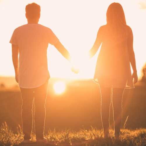 Zwei Menschen halten sich die Hand und schauen in den Sonnenuntergang.